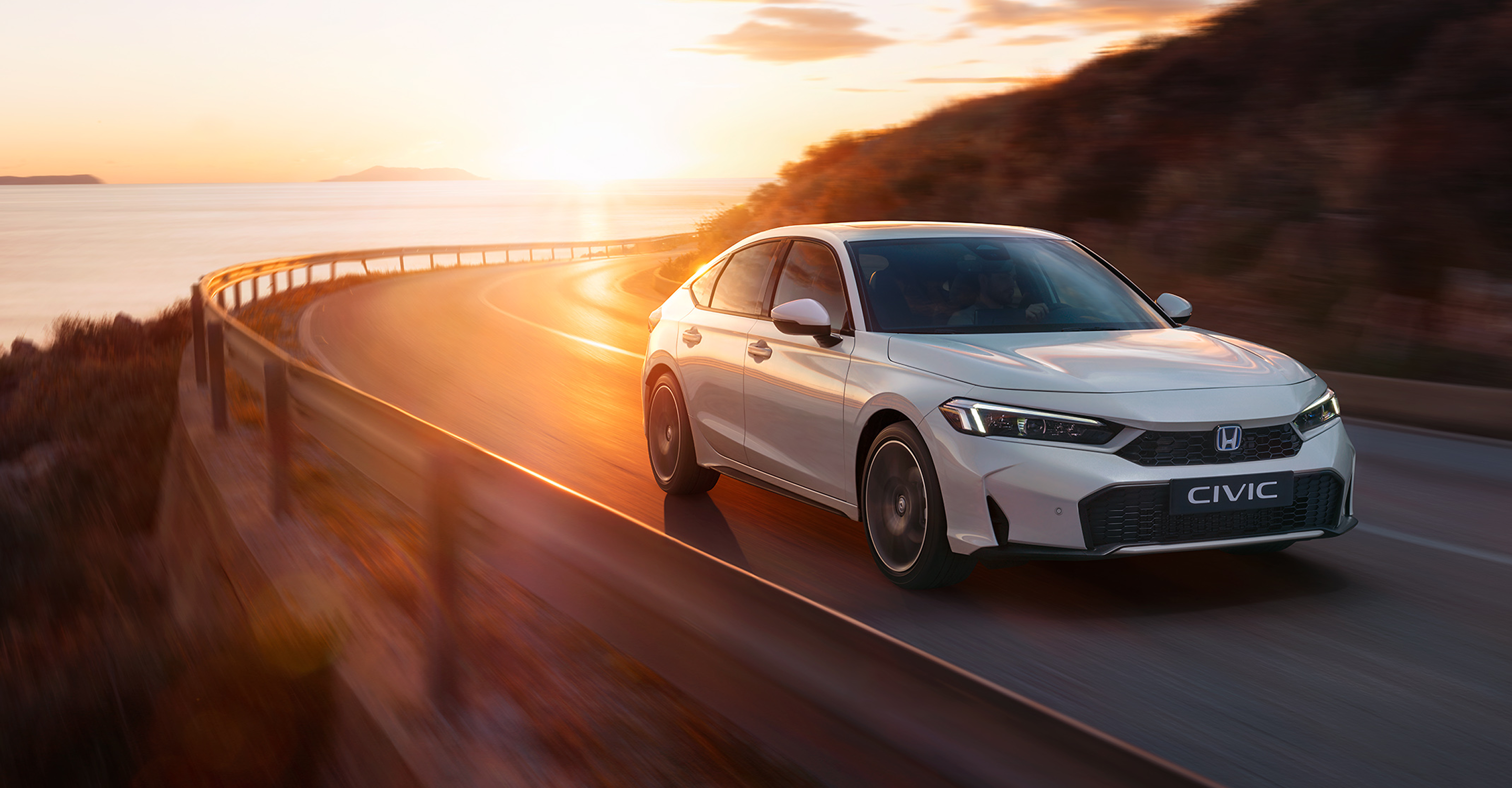 Ein weisser Civic Hybrid fährt auf einer Strasse, im Hintergrund sind der Sonnenuntergang und das Meer zu sehen