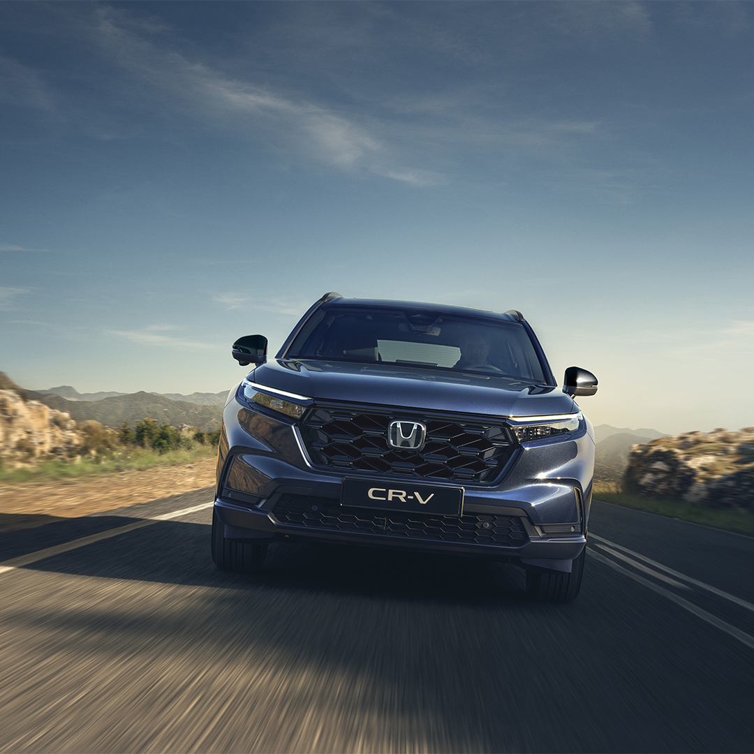 Un Honda CR-V roule sur une route de montagne sinueuse sous un ciel bleu azur.