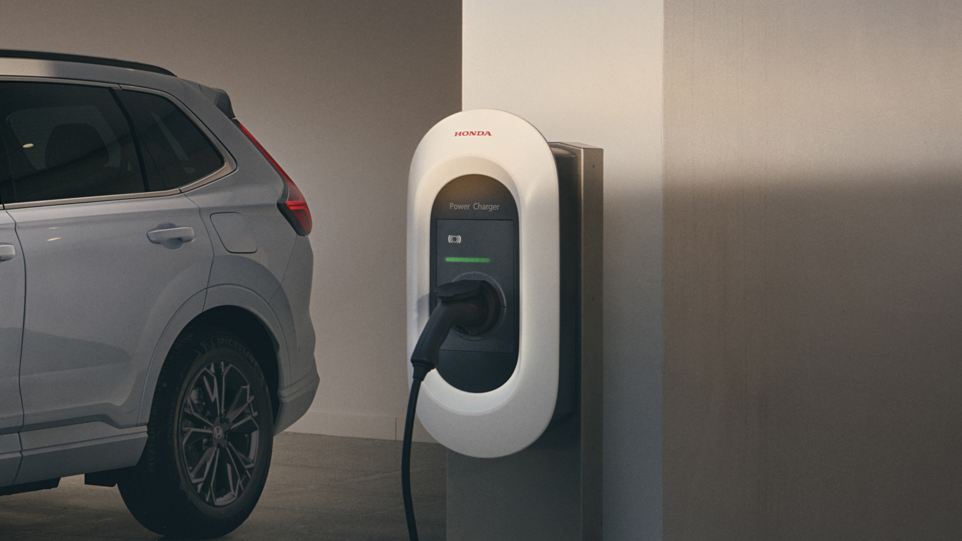 Une borne de recharge pour véhicules électriques Honda fixée au mur, avec un câble de recharge blanc branché à un CR-V Plug-in hybride blanc, vue de profil