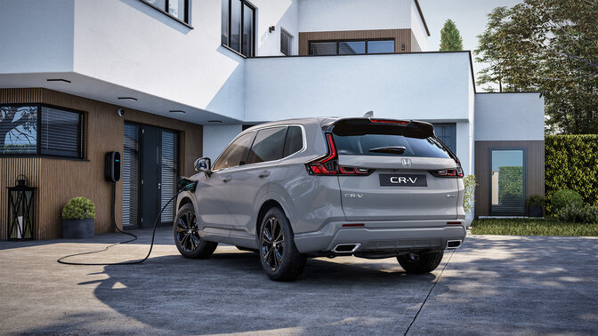 Vue de profil arrière du Honda CR-V hybride rechargeable blanc en train de charger à une borne à l'entrée d'une maison