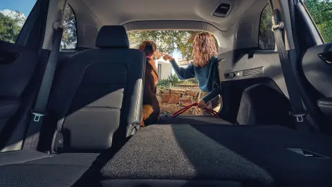 Siège arrière incliné du SUV hybride CR-V avec femme et chien dans le coffre ouvert. 