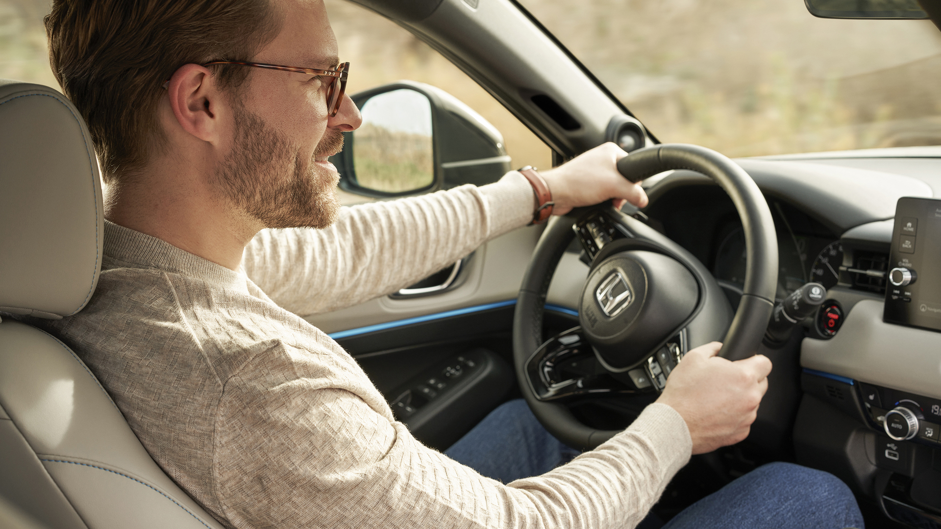 Un homme portant des lunettes conduit un Honda HR-V, vu depuis le siège passager avant, les deux mains sur le volant et la planche de bord visible.