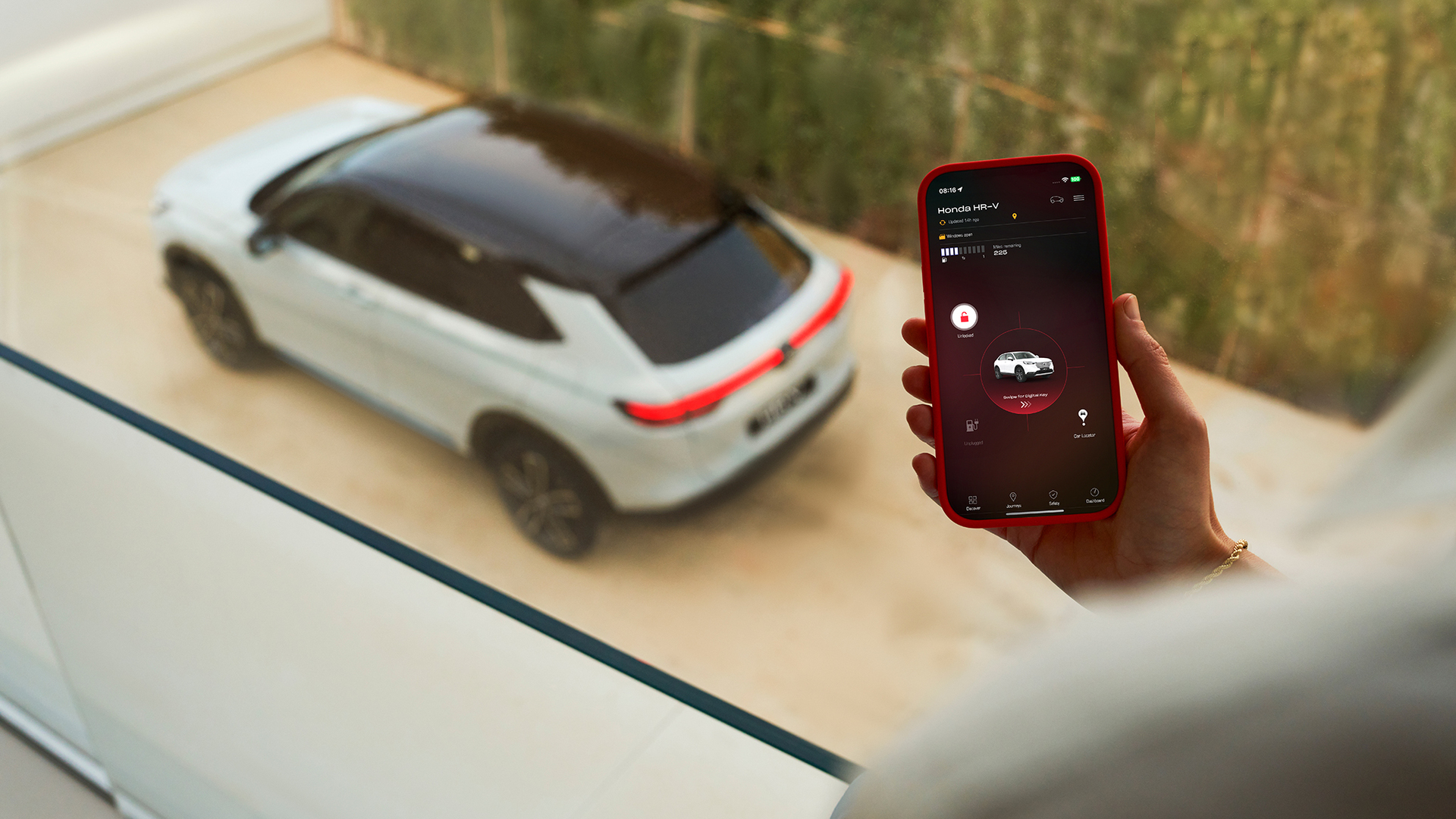 Une personne tient un smartphone affichant une application de gestion de la recharge du véhicule, tandis qu'un SUV blanc est garé en arrière-plan.