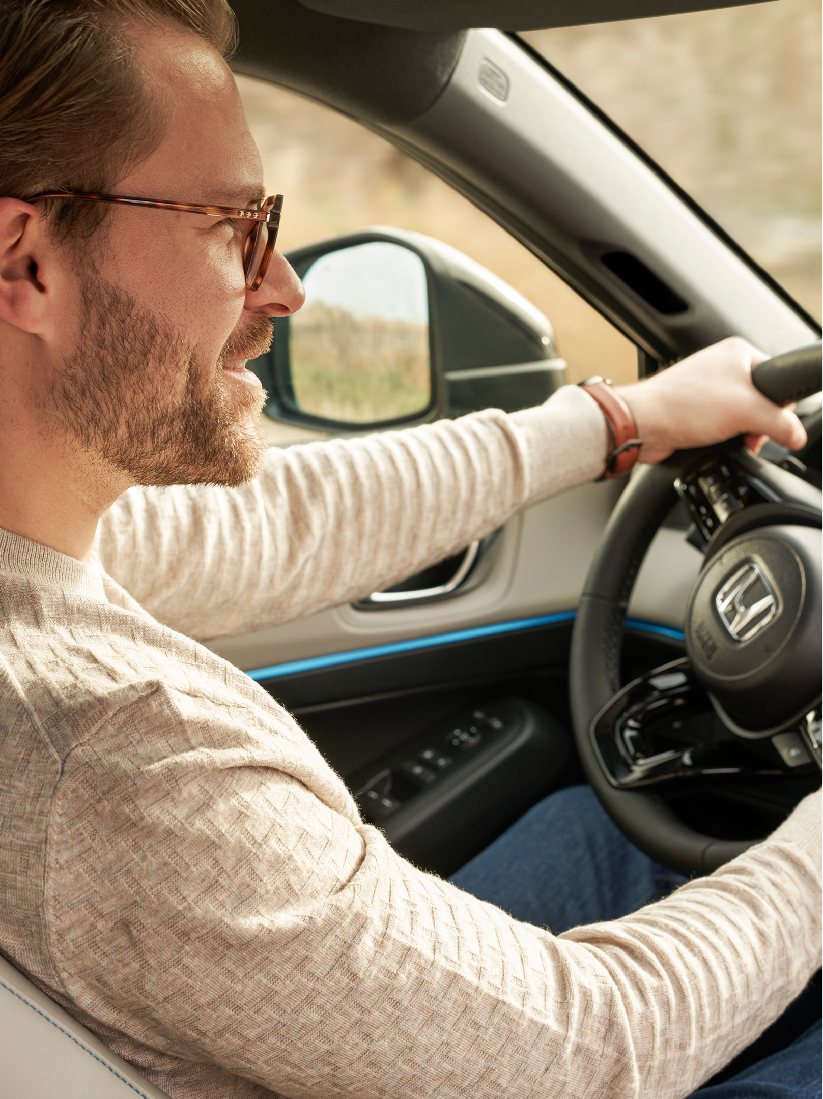 Un homme portant des lunettes conduit un Honda HR-V, vu depuis le siège passager avant, les deux mains sur le volant et la planche de bord visible.