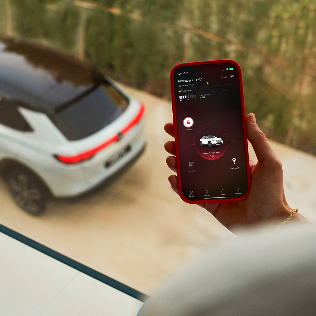 Une personne tient un smartphone affichant une application de gestion de la recharge du véhicule, tandis qu'un SUV blanc est garé en arrière-plan.