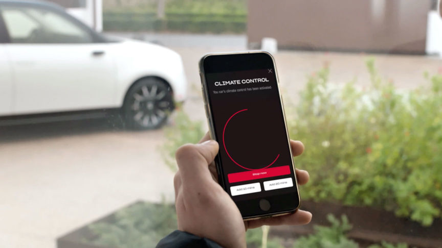 Homme regardant l'application My Honda Plus avec la Honda Jazz Hybrid Crosstar derrière. 