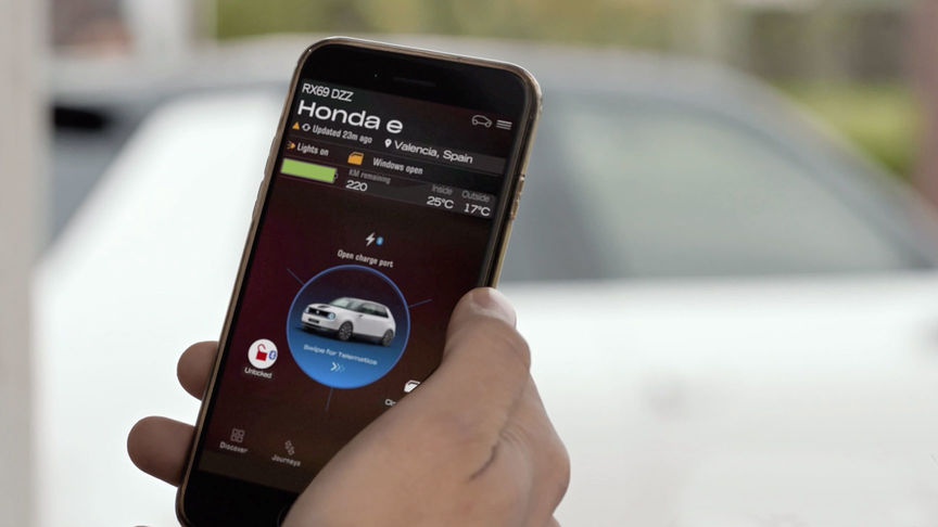 Homme regardant l'application My Honda Plus avec la Honda Jazz Hybrid Crosstar derrière. 