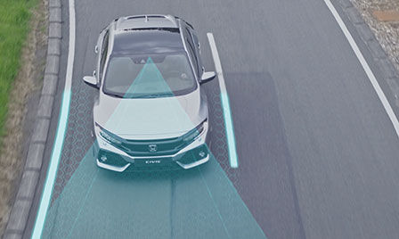 Cliché extérieur d'un véhicule à technologie Honda Sensing sur la route, avec mise en valeur des systèmes de prévention des collisions par freinage et d'assistance active au maintien dans la bande.