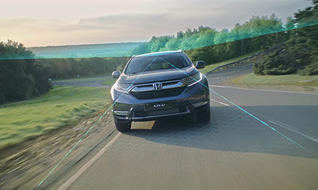 Véhicule à technologie Honda Sensing en campagne, avec mise en valeur des systèmes de prévention des sorties de route et de reconnaissance des panneaux de signalisation.