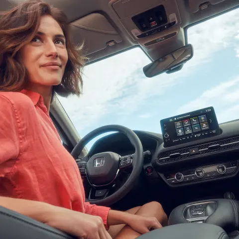 Femme assise sur siège conducteur utilisant l’écran d’infodivertissement du ZR-V hybride de Honda.