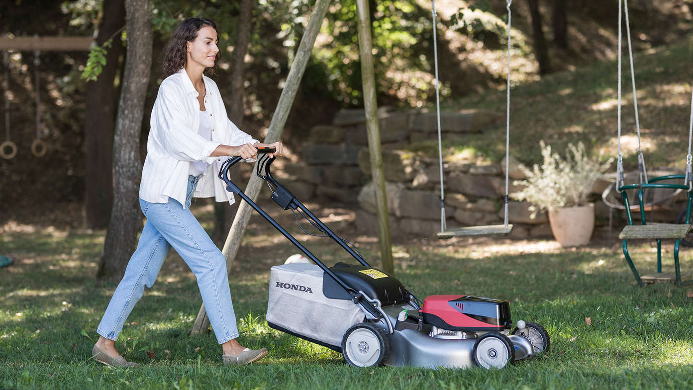Model using Honda's cordless lawn mower in garden location.