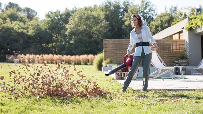 Model using Honda cordless leaf blower in garden location.