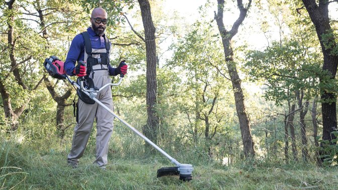 Front-three quarter view of brushcutter with model in a field.