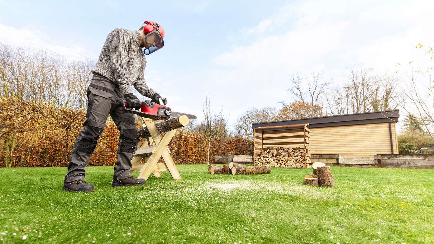 Homme utilisant une tronçonneuse sans fil dans un jardin.