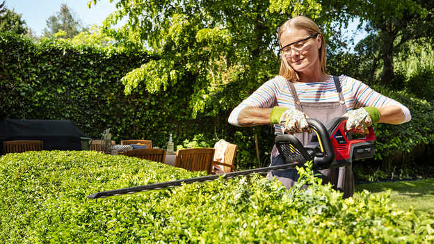 Femme taillant une haie avec un taille-haies à batterie Honda dans un jardin.