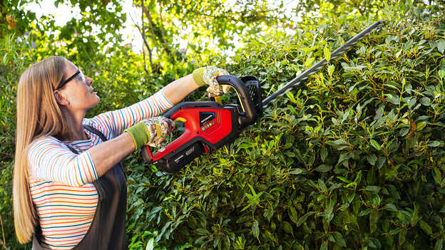 Femme taillant des buissons avec un taille-haies à batterie Honda dans un jardin.