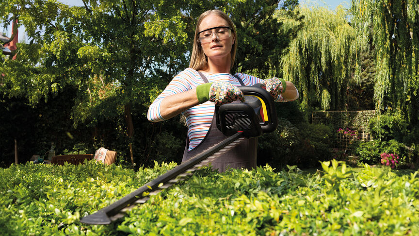 Femme taillant une haie dans un jardin avec un taille-haies à batterie Honda.