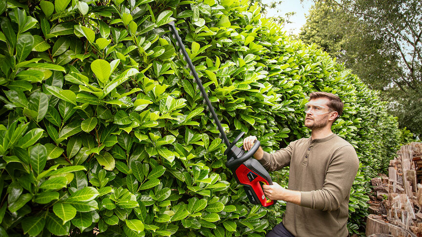 Femme taillant une haie dans un jardin avec un taille-haies à batterie Honda.