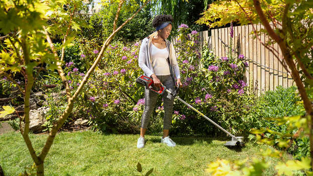 Utilisateur avec un coupe-bordure batterie Honda dans un jardin.