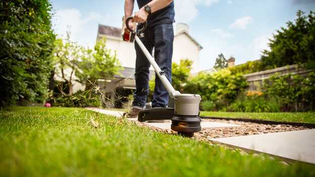 Utilisateur avec un coupe-bordure batterie Honda dans un jardin.