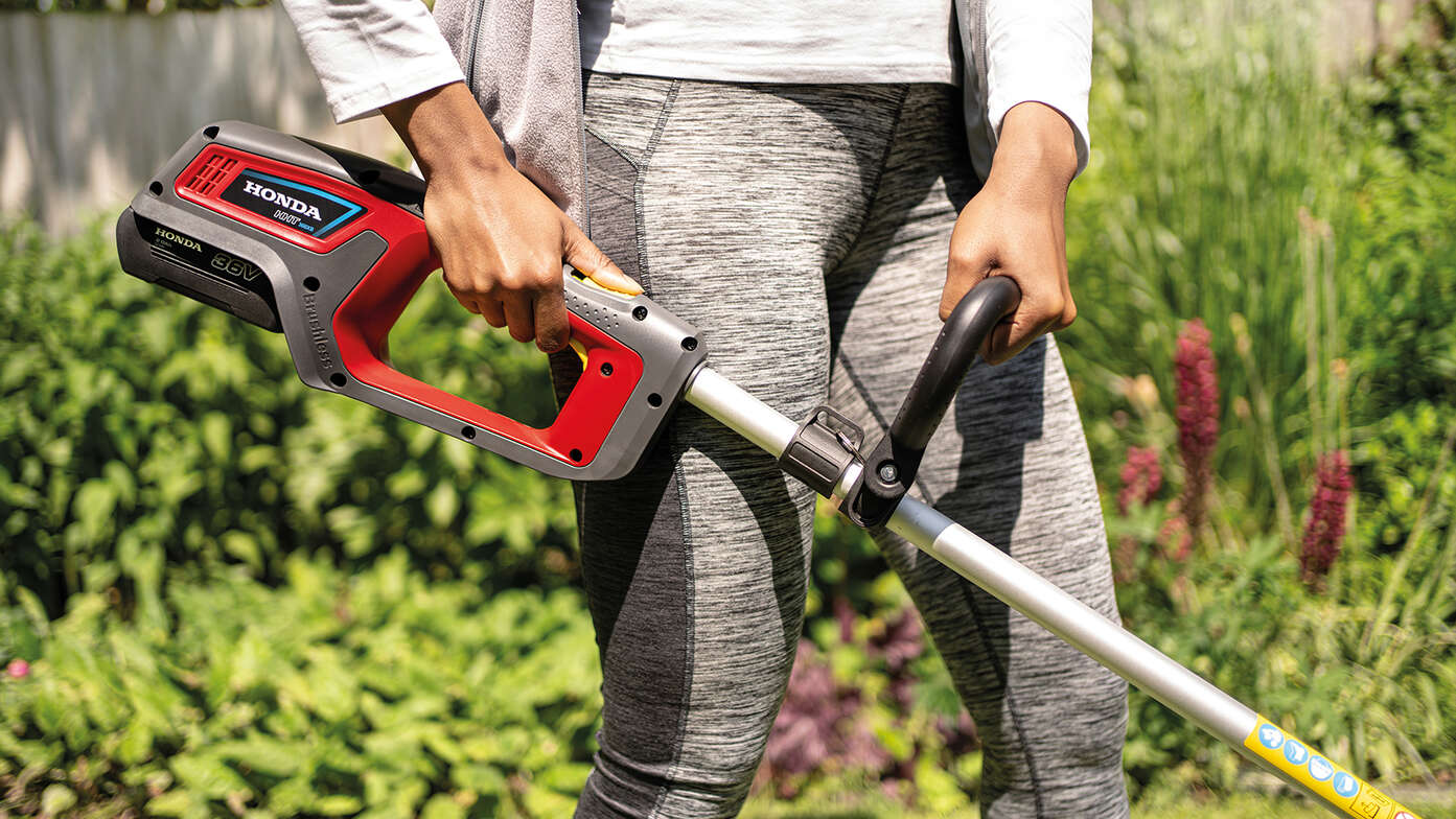 Utilisateur avec un coupe-bordure batterie Honda dans un jardin.