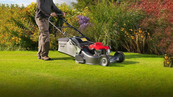 Homme avec tondeuse à gazon Honda HRH coupant l'herbe dans le jardin