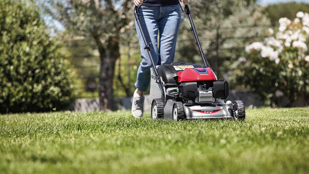 Vue latérale de la tondeuse à gazon Honda IZY avec une femme dans le jardin