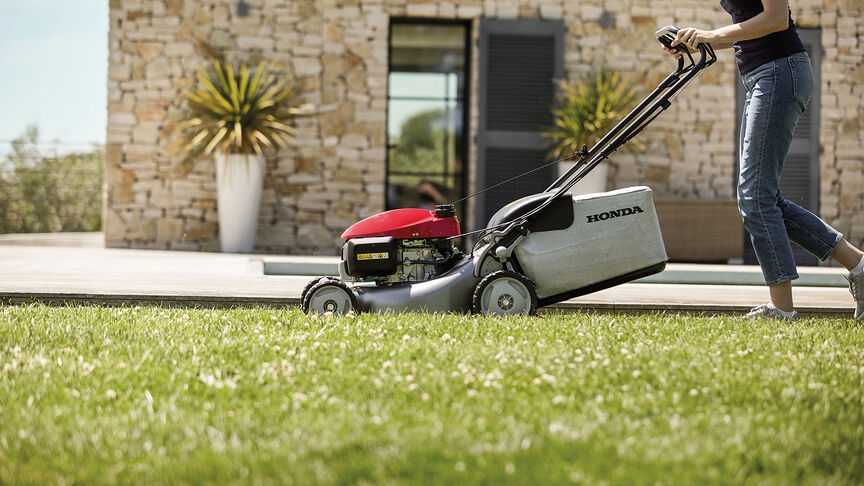 Vue latérale de la tondeuse à gazon Honda IZY avec une femme dans le jardin