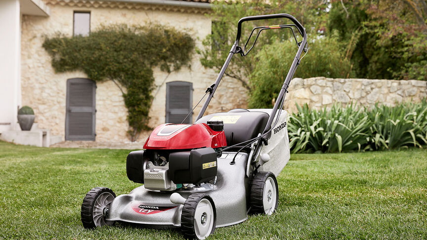 Vue latérale de la tondeuse à gazon Honda IZY avec une femme dans le jardin