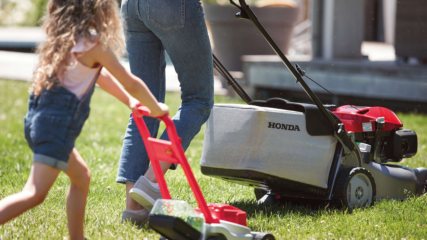 Vue latérale de la tondeuse à gazon Honda IZY avec un enfant dans le jardin