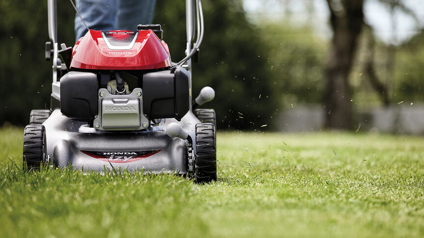 Vue latérale de la tondeuse à gazon Honda IZY avec une femme dans le jardin