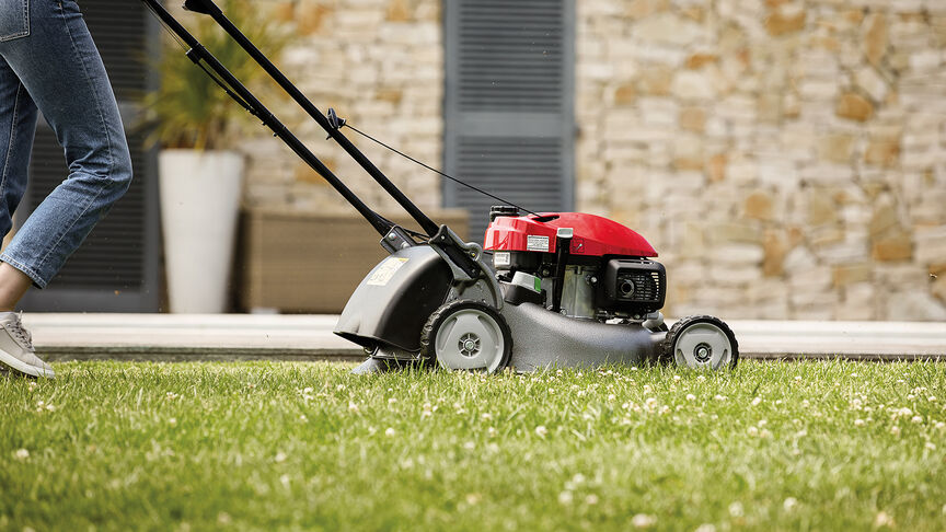 Vue latérale de la tondeuse à gazon Honda IZY avec une femme dans le jardin