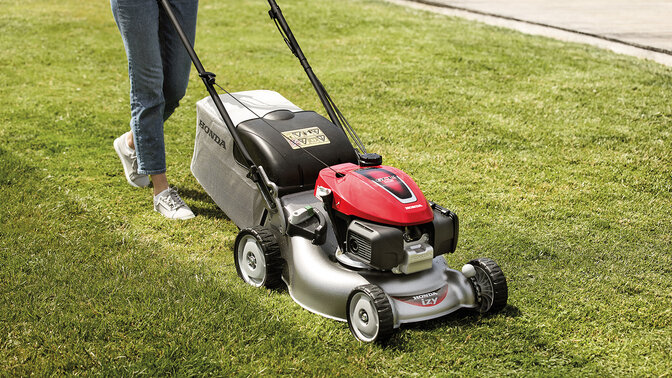 Dame avec tondeuse à gazon Honda IZY coupant l'herbe dans le jardin