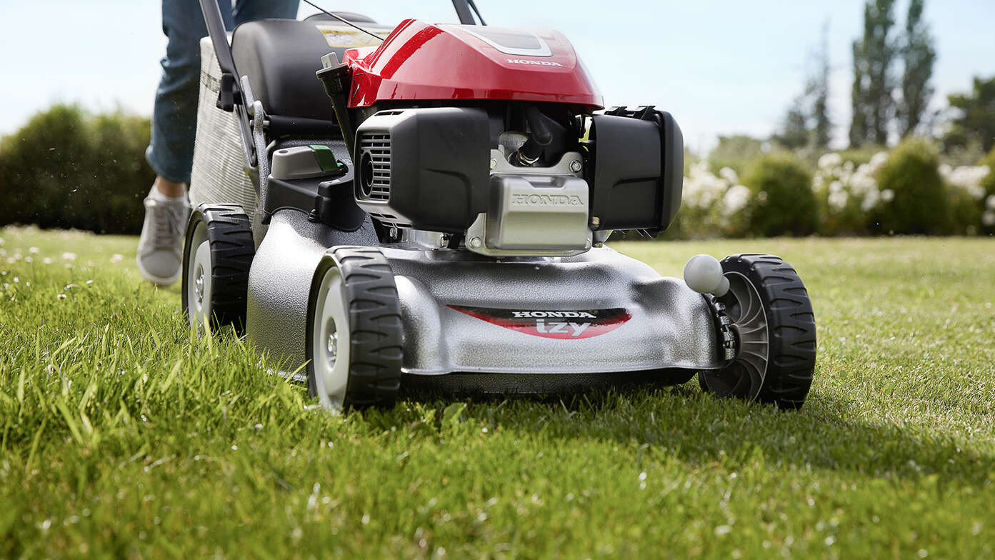 Vue latérale de la tondeuse à gazon Honda IZY avec une femme dans le jardin