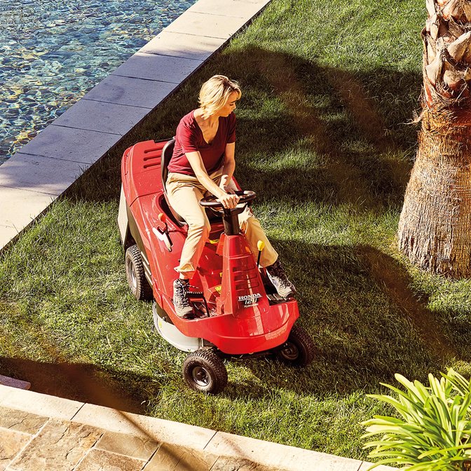 Tondeuse autoportée, de trois quarts face, tournée vers la gauche, utilisée par un démonstrateur, dans un jardin.