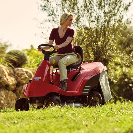 Tondeuse autoportée, de trois quarts face, tournée vers la droite, utilisée par un démonstrateur, dans un jardin.