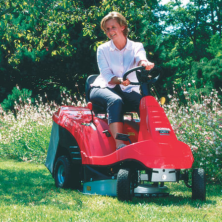 Tondeuse autoportée, de trois quarts face, utilisée par un démonstrateur, dans un jardin.