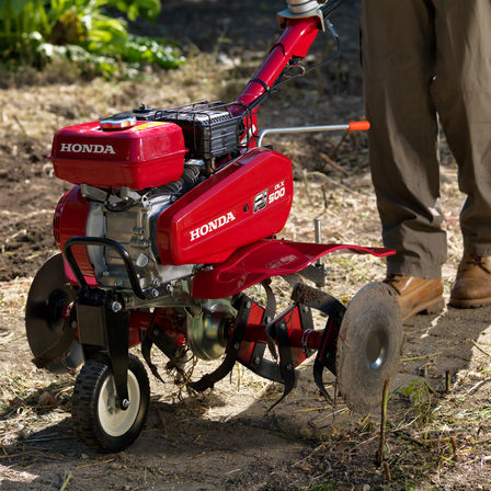 Gros plan de la motobineuse compacte, mettant en évidence la roue de transport, dans un jardin.