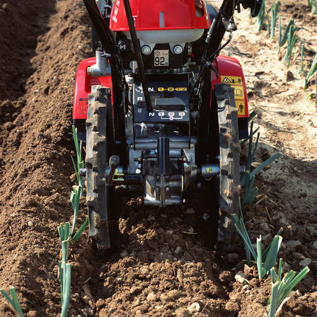 Gros plan de la motobineuse équipée d'outils rotatifs dans un jardin.