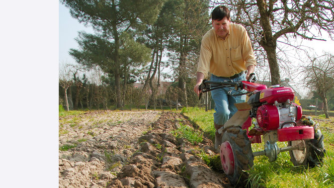 Motoculteur transformable utilisé par un démonstrateur dans un jardin.