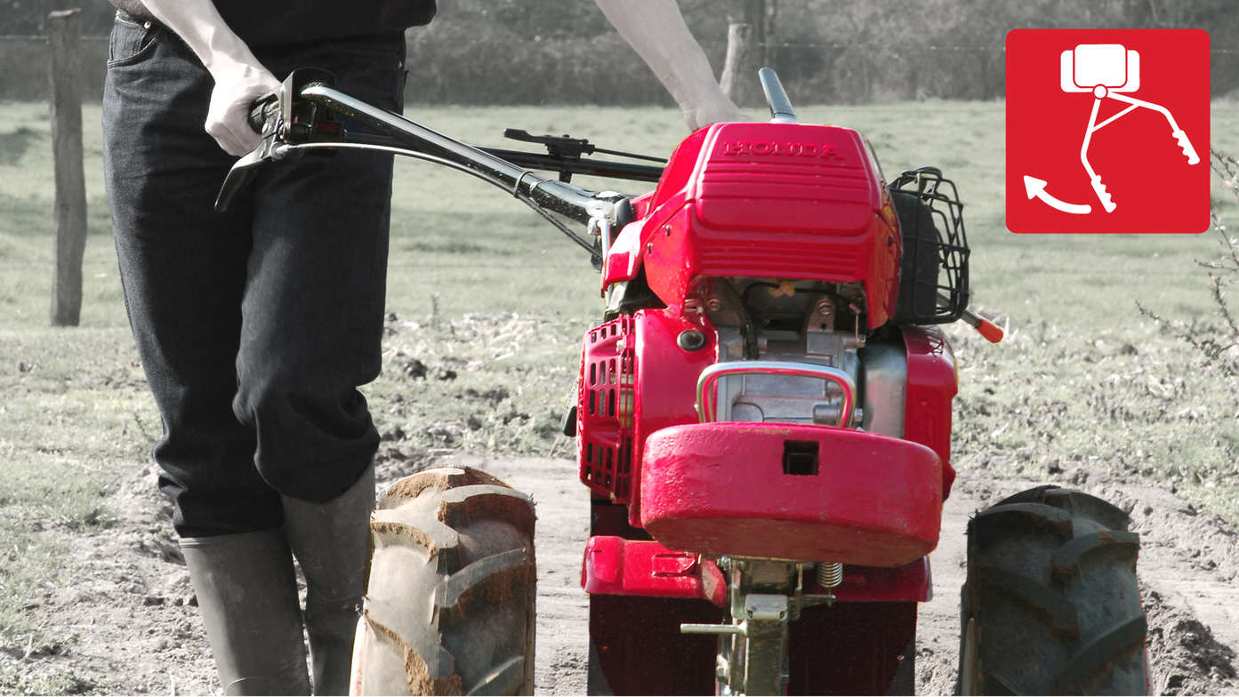 Motoculteur transformable, mettant en évidence le guidon déportable dans un jardin.