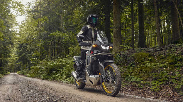 Modèle conduisant une Honda XL750 Transalp dans une forêt.