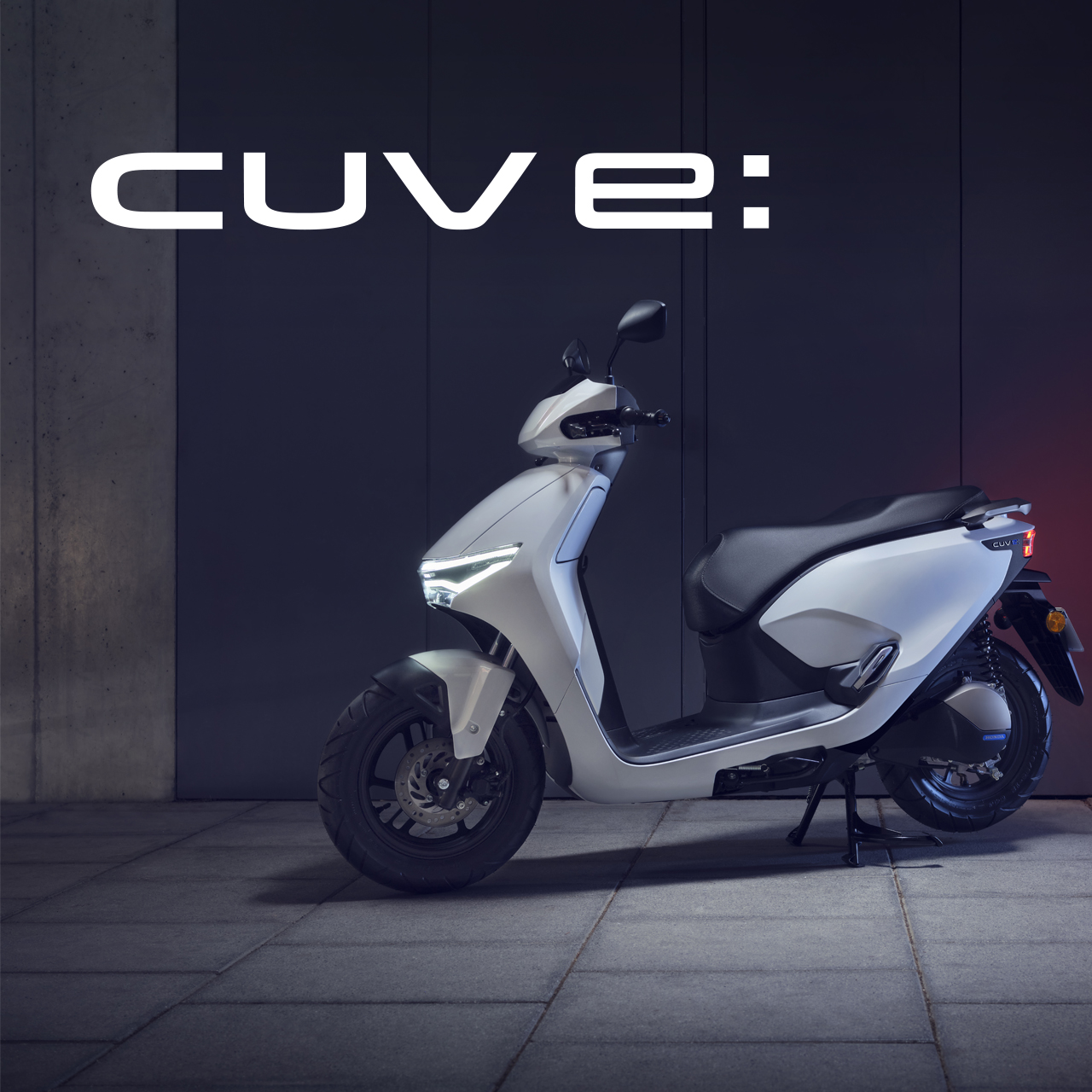 A white Honda Cuve: electric scooter parked against a dark background. The scooter has a sleek, modern design with a large text \"CUVE:\" displayed above it.