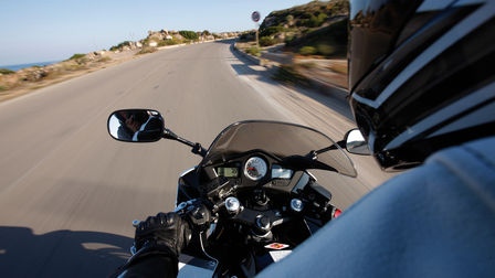 Vue par-dessus l'épaule du conducteur des instruments de la moto, du guidon et de la route (en situation).