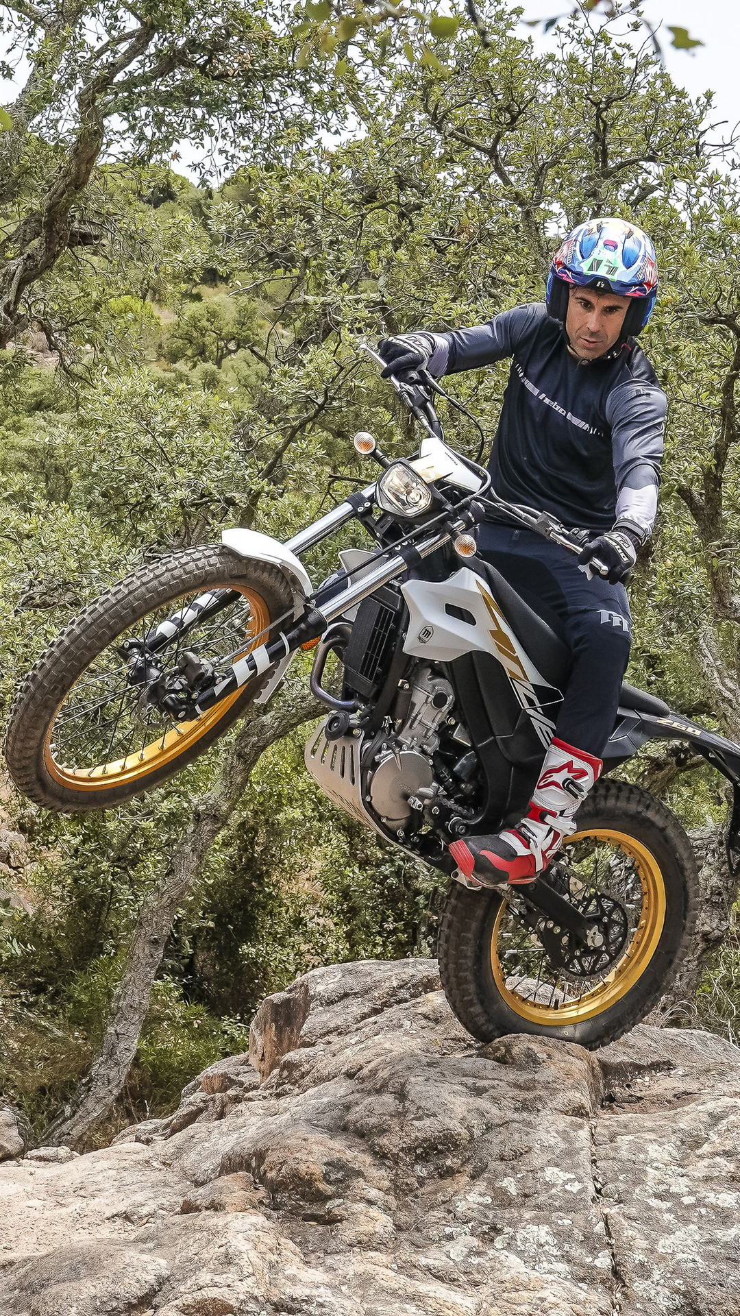 Pilote levant la roue avant d’une Montesa 4RIDE sur un chemin forestier rocailleux.