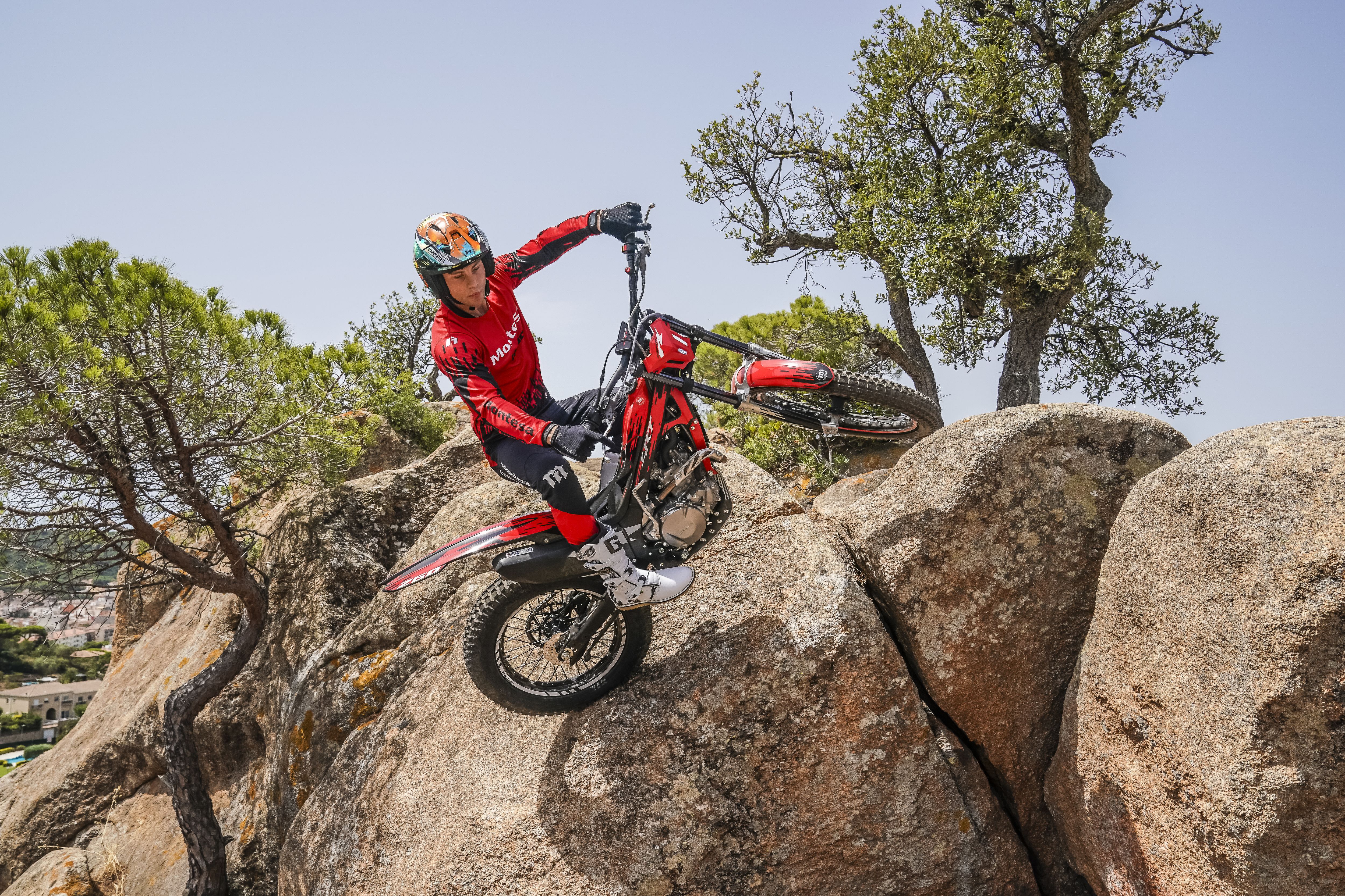 Pilote franchissant de gros rochers en montée avec une Montesa Cota 4RT 260R rouge, par temps ensoleillé.