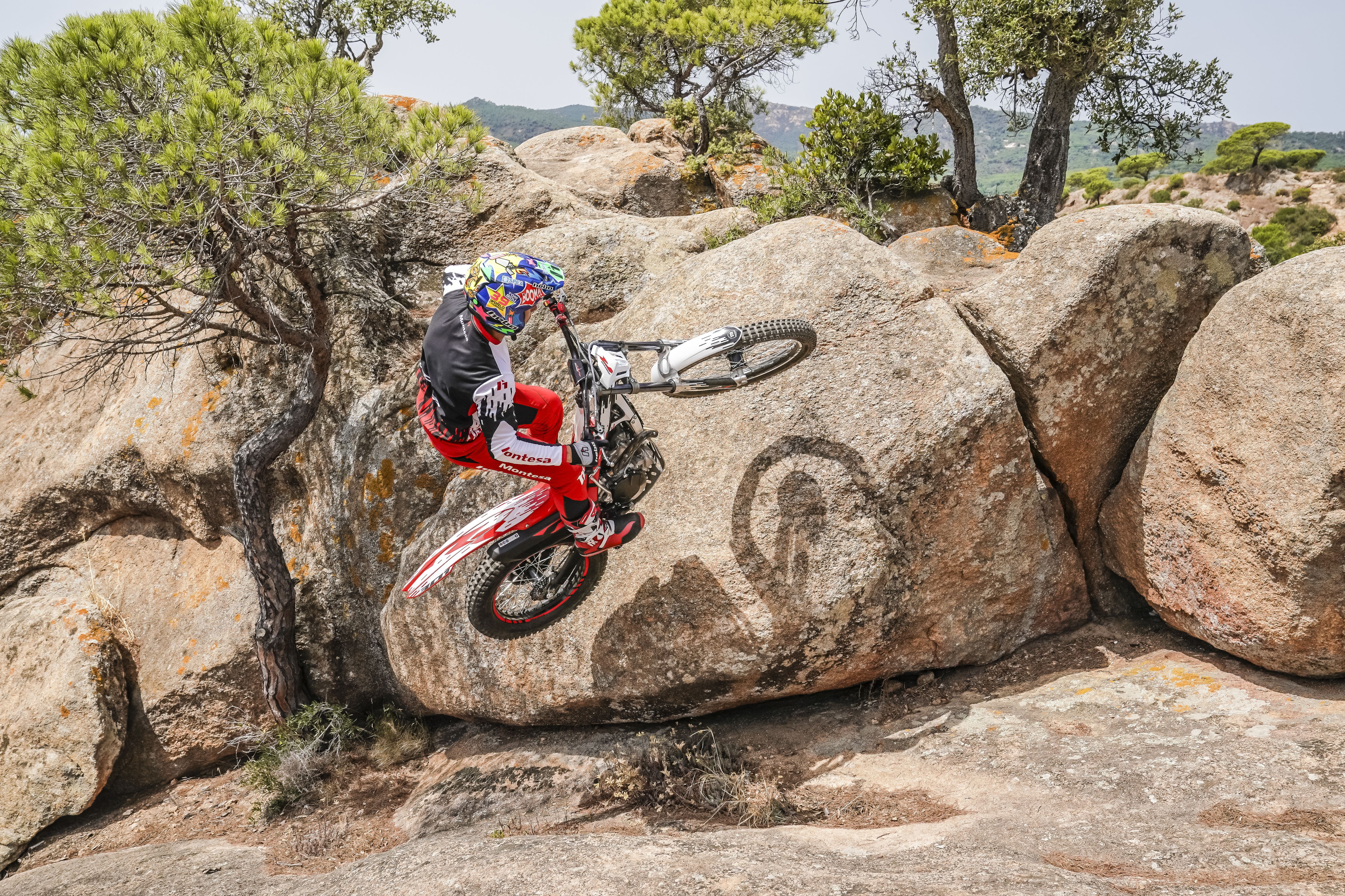 Pilote réalisant un wheeling avec une Montesa Cota 301RR sur une formation rocheuse.