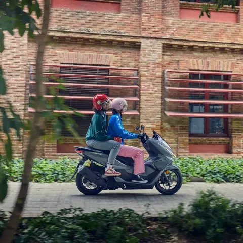 Plan latéral de mannequins à bord de la moto PCX125 en milieu urbain.