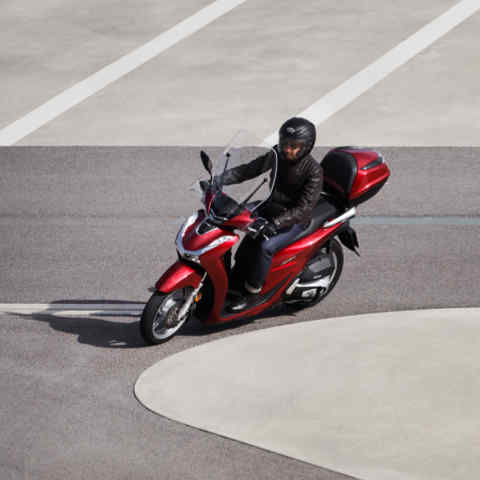 scooter grandes roues Honda SH125i, vue de trois quarts avant gauche, avec conducteur qui opère un virage à gauche sur une route