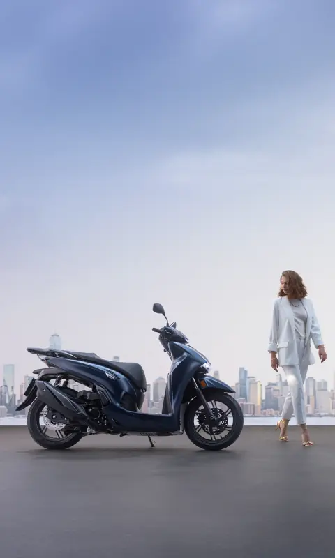 Femme debout à côté d'une Honda SH350i en ville.